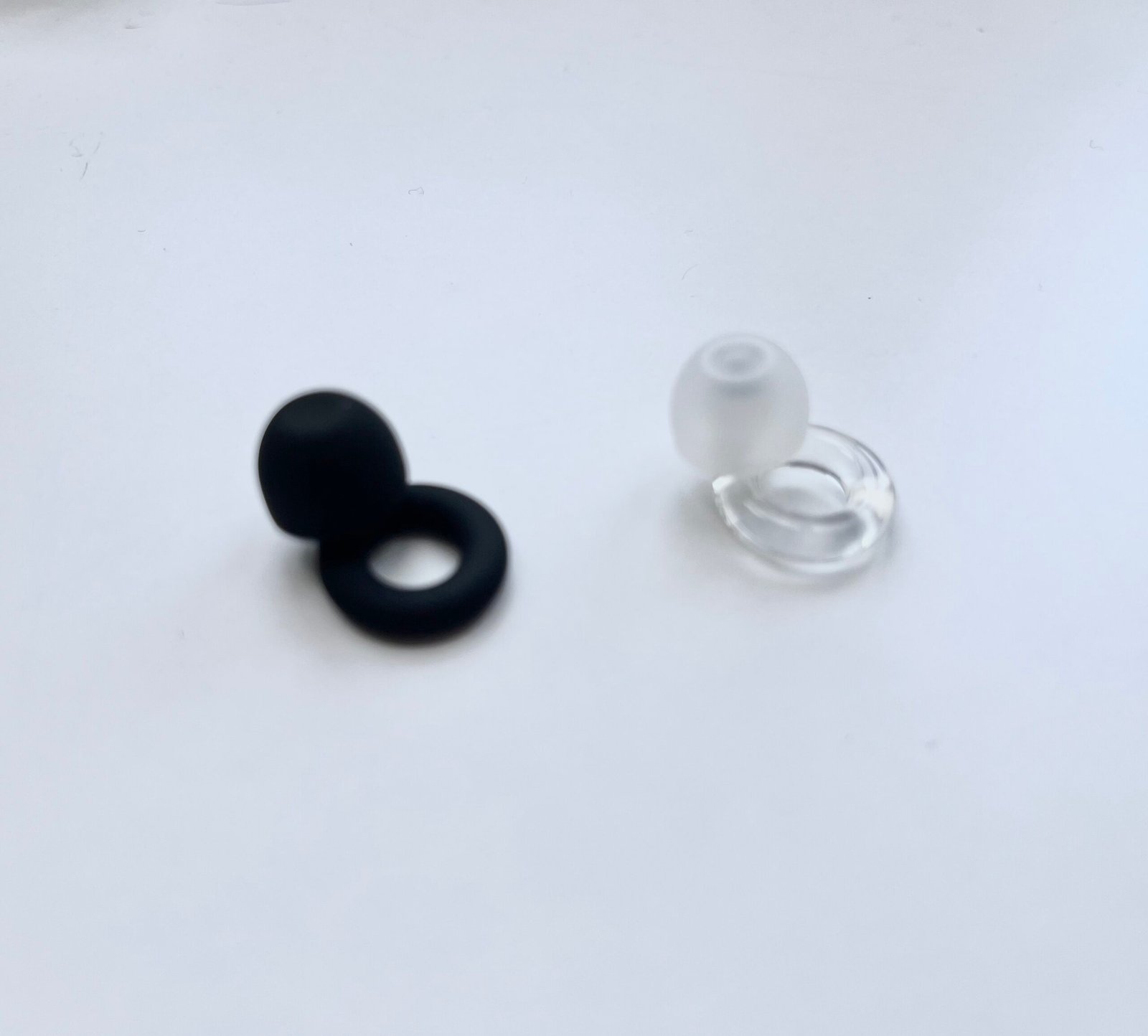 Loop Quiet 2 and Loop Engage earplugs placed side by side on a pale paper surface, showing identical housing with different internal filter visible on the transparent Engage model.