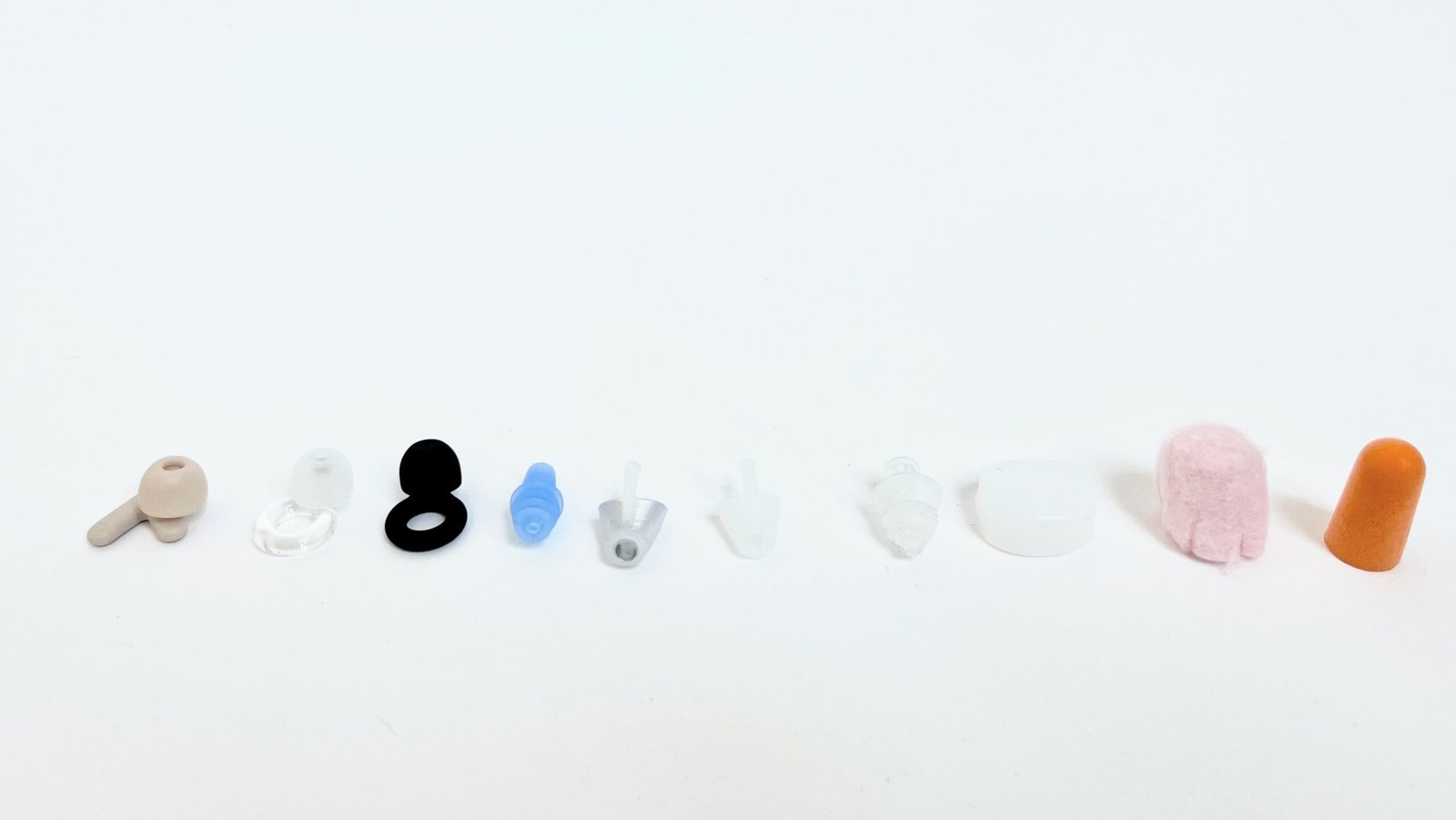 All ten earplug products laid out on a clean surface — foam, silicone, wax, and hollow resonance modifiers