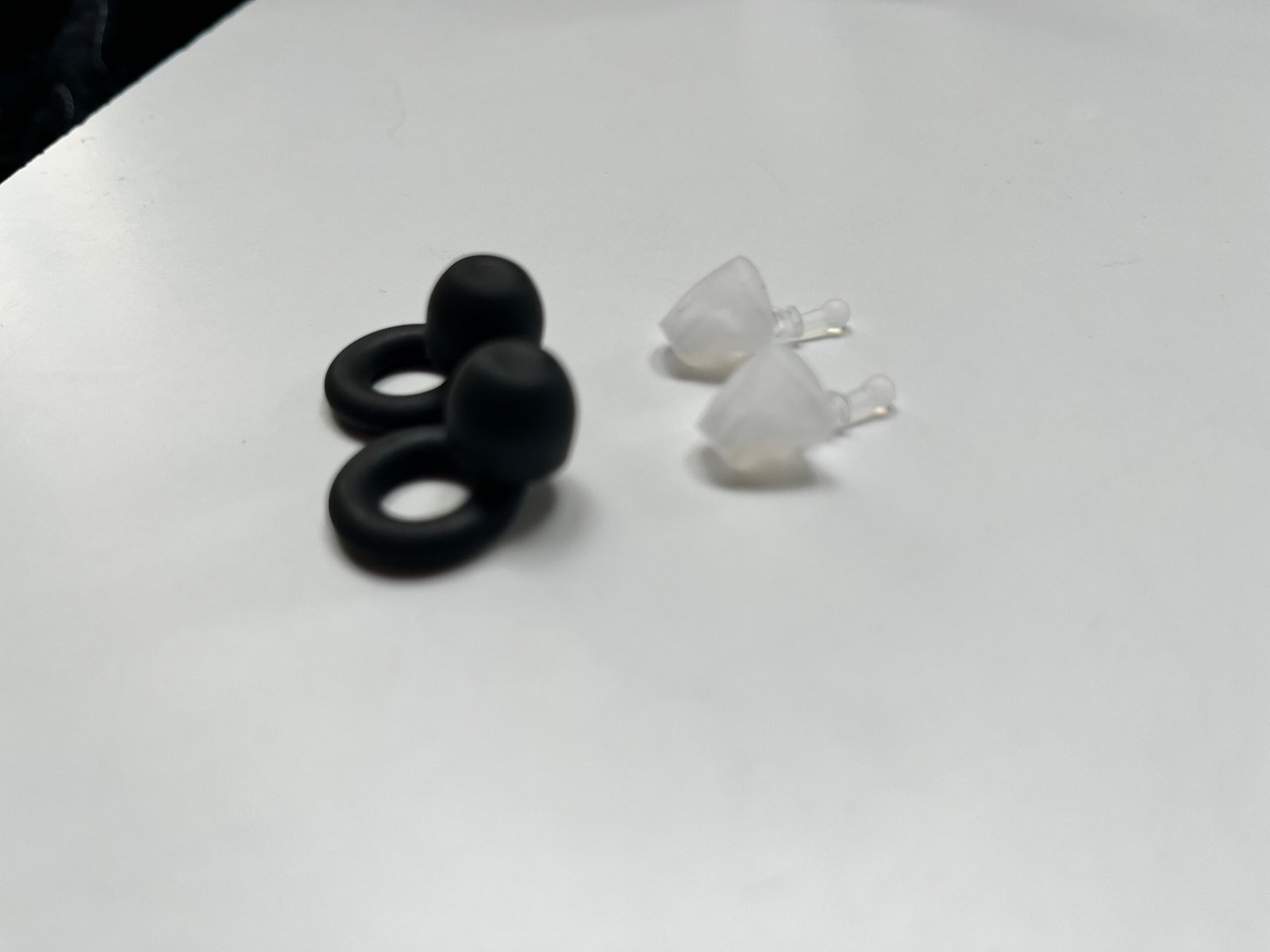 Loop Quiet 2 and Flare Calmer earplugs side by side. The Quiet 2 is a ring-stemmed silicone plug that seals the canal; the Flare Calmer is an open device that sits in ear blocking some sound when the filters are inserted.